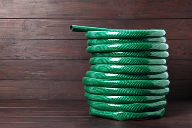 Green garden hose on wooden table, space for text