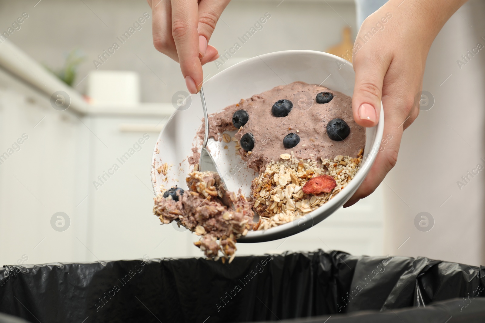 Photo of Woman throwing oatmeal with berries into bin indoors, closeup