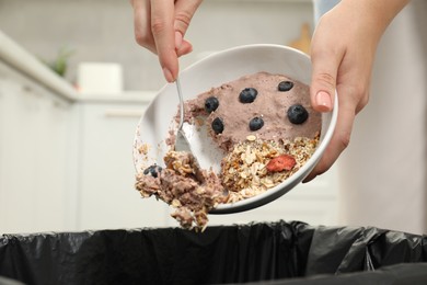 Woman throwing oatmeal with berries into bin indoors, closeup