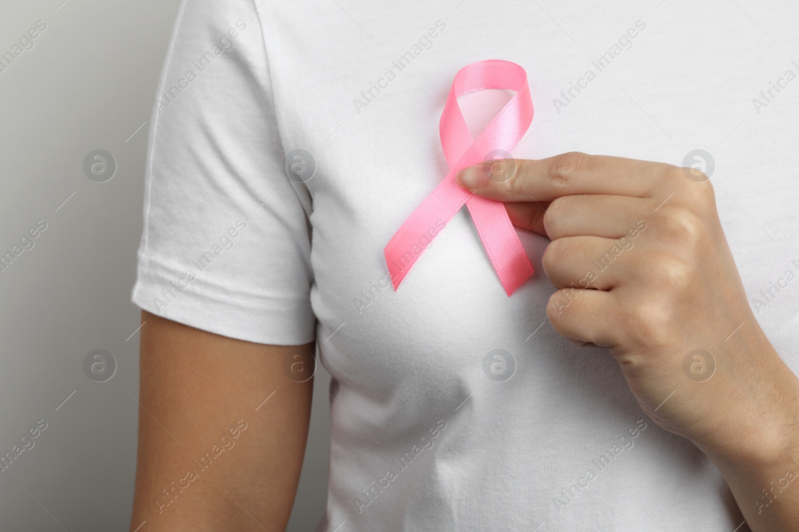 Photo of Woman holding pink ribbon on grey background, closeup. Breast cancer awareness