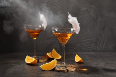 Tasty cocktails in glasses decorated with cotton candy and orange slices on gray table