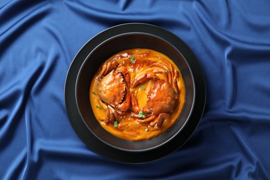 Photo of Delicious boiled crabs with sauce in bowl on blue tablecloth, top view