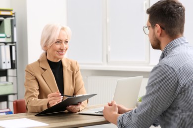 Happy woman with clipboard and man at wooden table in office. Manager conducting job interview with applicant