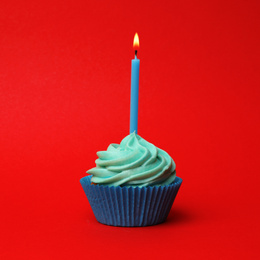 Delicious birthday cupcake with turquoise cream and burning candle on red background