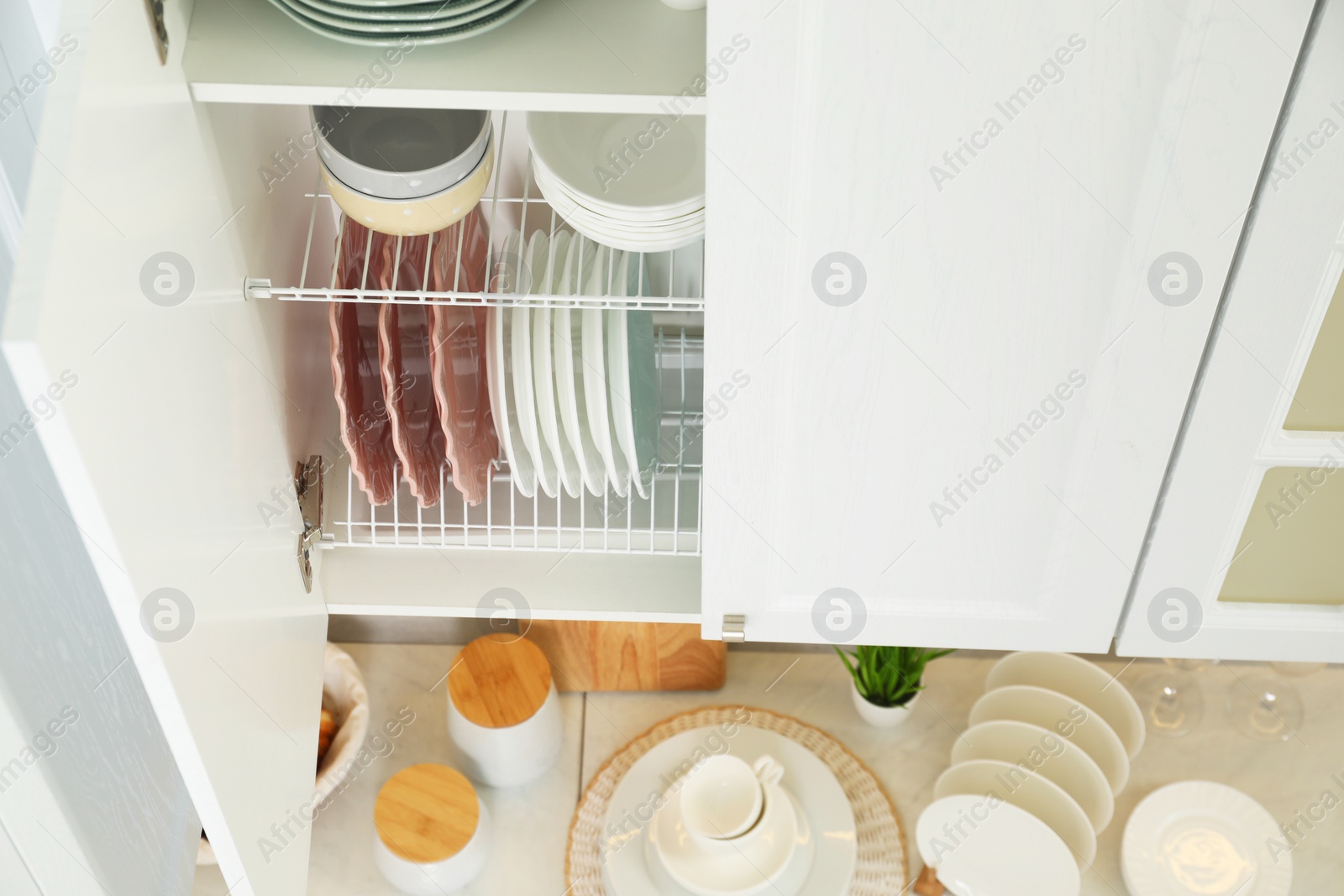 Photo of Clean plates and bowls on shelves in cabinet indoors