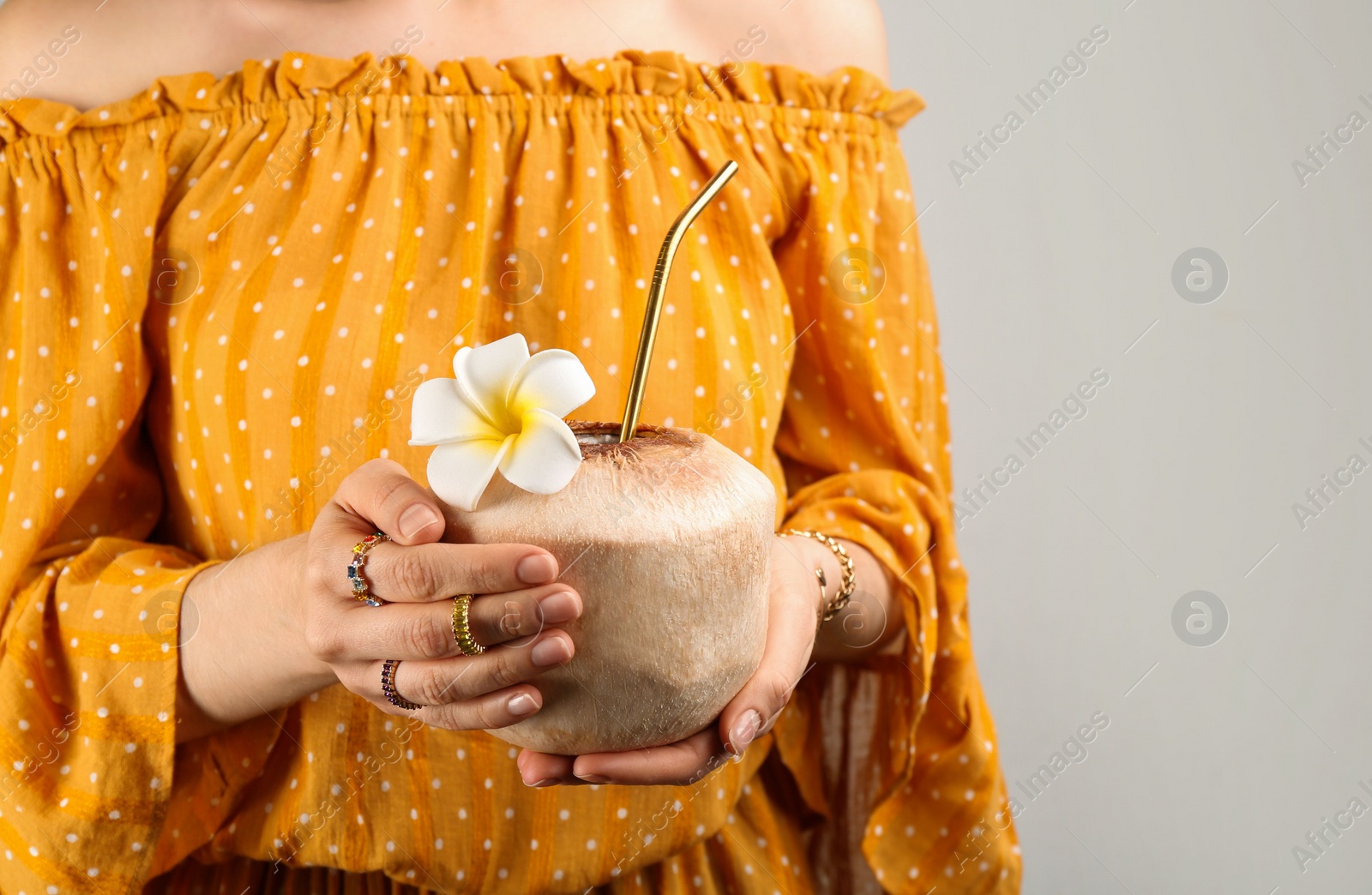 Photo of Woman holding fresh young coconut with straw on grey background, closeup