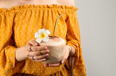 Woman holding fresh young coconut with straw on grey background, closeup