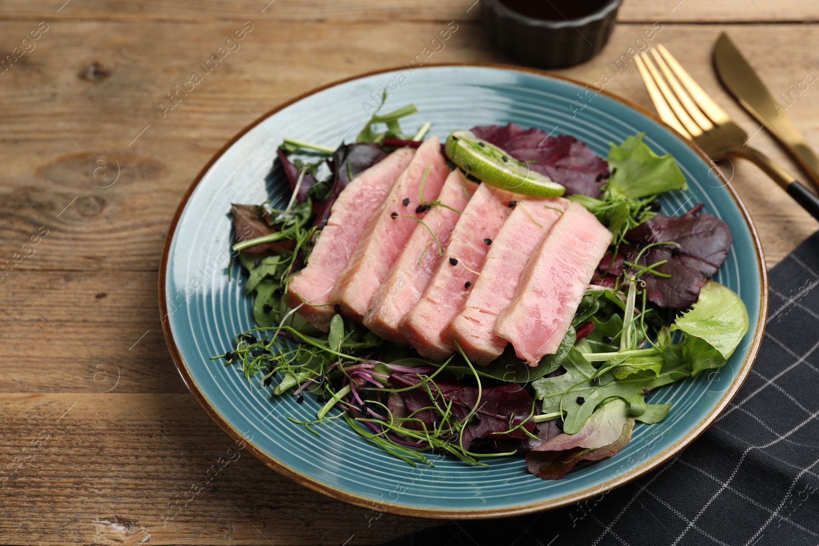 Photo of Pieces of delicious tuna steak with salad served on wooden table, closeup