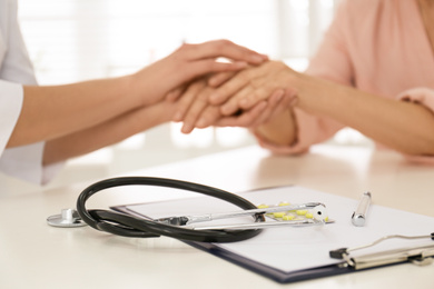 Closeup view of doctor holding senior patient's hands in office, focus on stethoscope