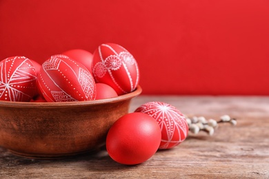 Photo of Wooden bowl with red painted Easter eggs on table against color background, space for text