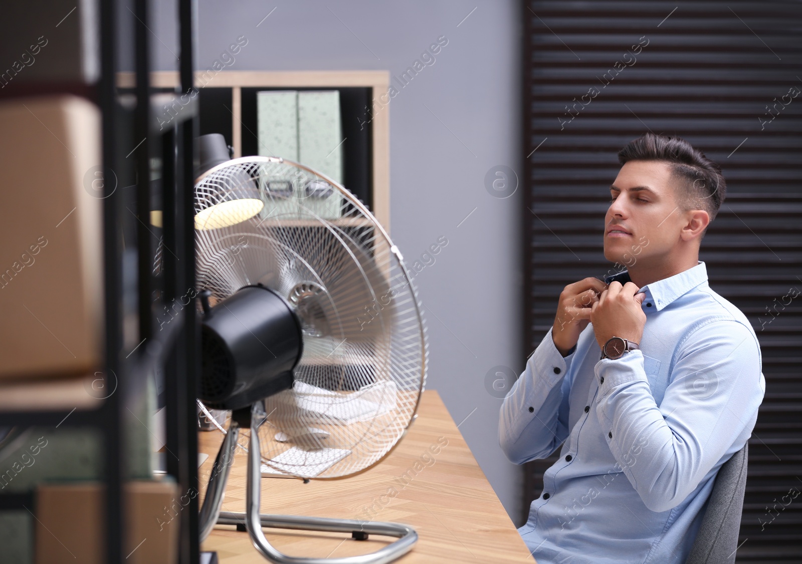 Photo of Man enjoying air flow from fan at workplace