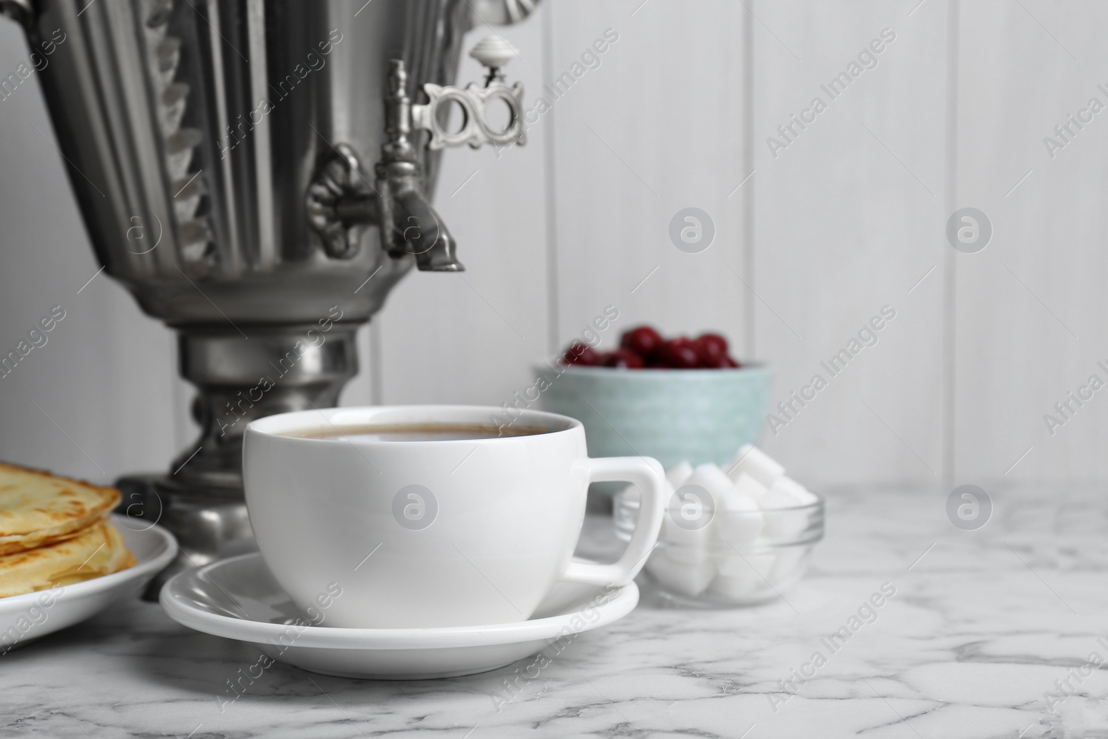 Photo of Metal samovar with cup of tea and treats on white marble table, space for text