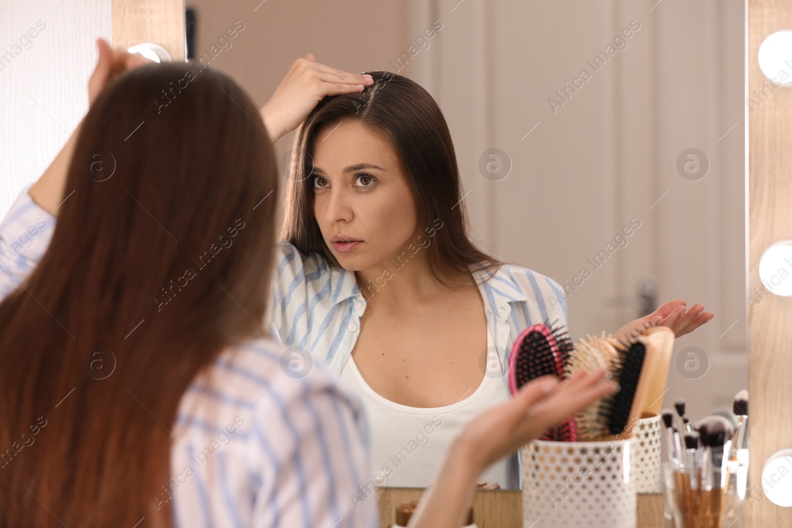 Photo of Young woman with hair loss problem looking in mirror indoors