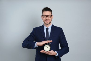Photo of Happy businessman holding alarm clock on grey background. Time management