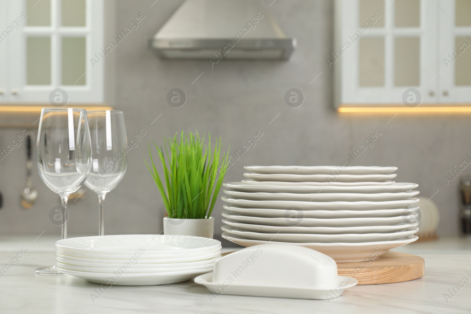 Photo of Clean plates, glasses, butter dish and floral decor on white marble table in kitchen