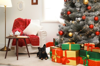Photo of Adorable dog in room with decorated Christmas tree. Festive interior