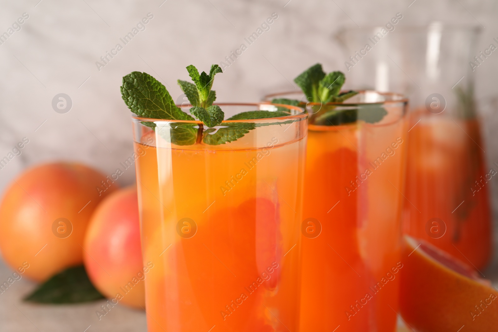 Photo of Tasty freshly made grapefruit juice with mint on table, closeup