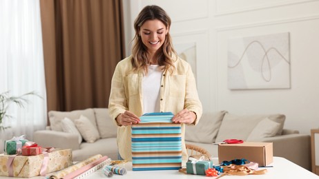 Photo of Beautiful young woman wrapping gift at table in living room