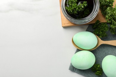 Turquoise Easter eggs painted with natural dye and curly parsley on white table, flat lay. Space for text