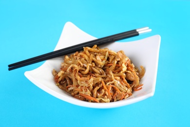 Plate with Chinese noodles and chopsticks on color background. Food delivery