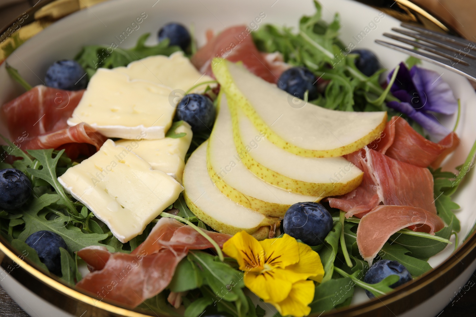 Photo of Tasty salad with brie cheese, prosciutto, blueberries and pear in bowl, closeup