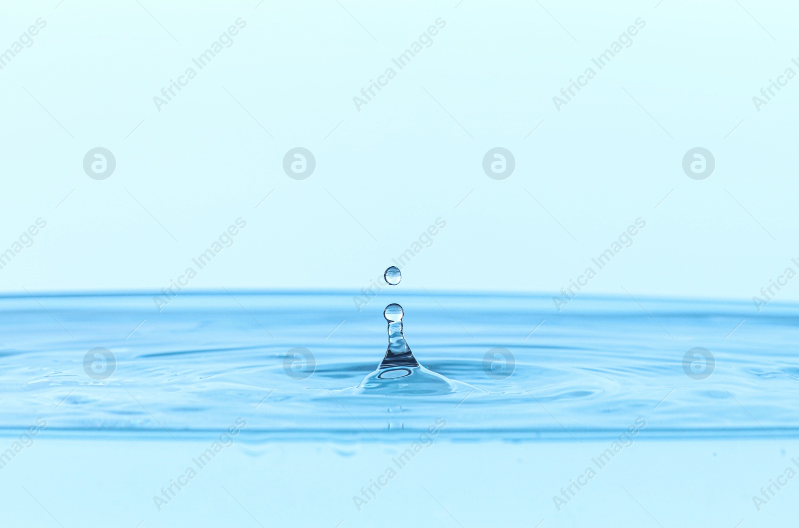 Photo of Splash of clear water with drop on light blue background, closeup