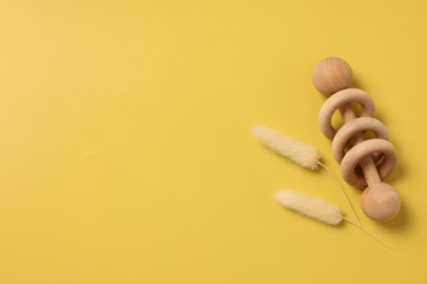 Photo of Baby accessory. Wooden rattle and dry spikes on yellow background, top view. Space for text