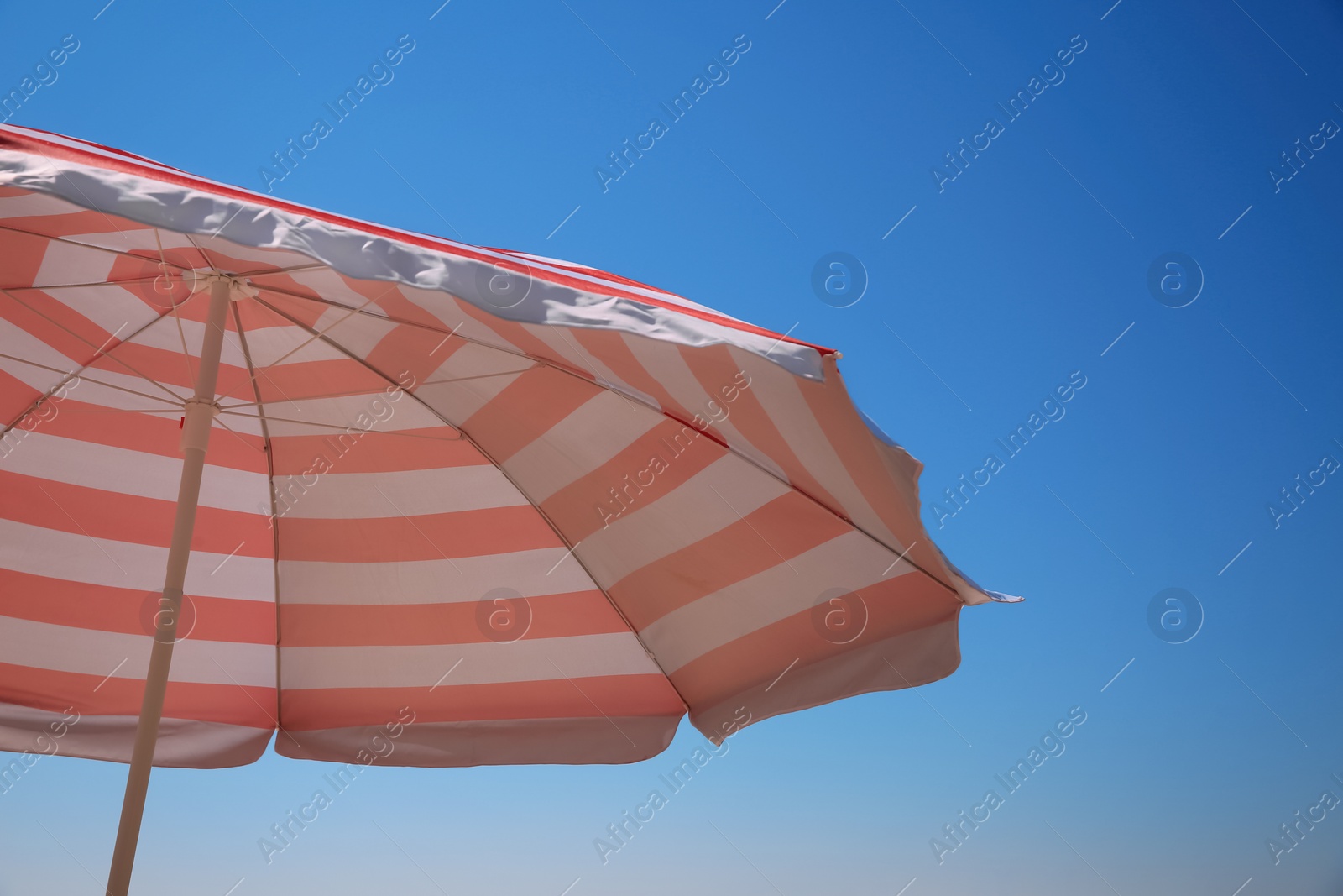 Photo of Red and white striped beach umbrella against blue sky, space for text