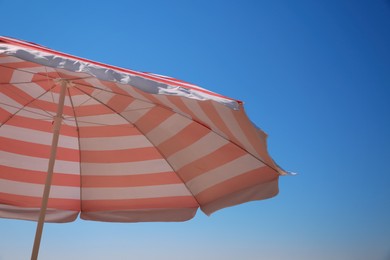 Red and white striped beach umbrella against blue sky, space for text