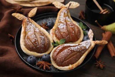 Delicious pears baked in puff pastry with powdered sugar served on wooden table, closeup