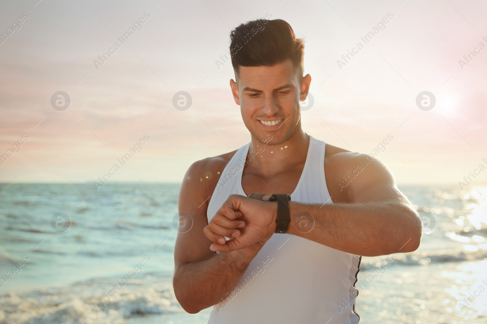 Photo of Man with athletic body checking fitness bracelet on beach
