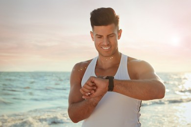Photo of Man with athletic body checking fitness bracelet on beach