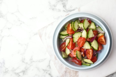 Photo of Bowl of vegetarian salad with cucumber, tomato and onion on marble background, top view. Space for text