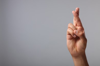 Photo of Man crossing his fingers on grey background, closeup. Space for text