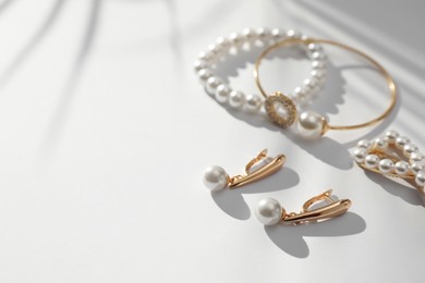 Photo of Elegant bracelets, hair clip and earrings with pearls on white table, closeup. Space for text