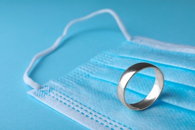 Photo of Wedding ring and medical mask on light blue background, space for text. Divorce during coronavirus outbreak