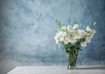 Photo of Vase with beautiful Eustoma flowers on table against color background