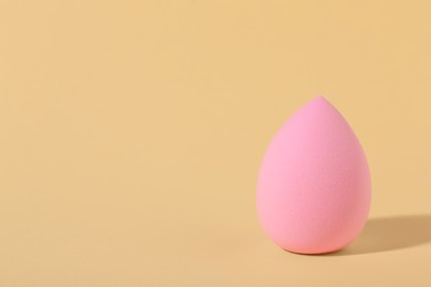 Photo of Pink makeup sponge on beige background, space for text