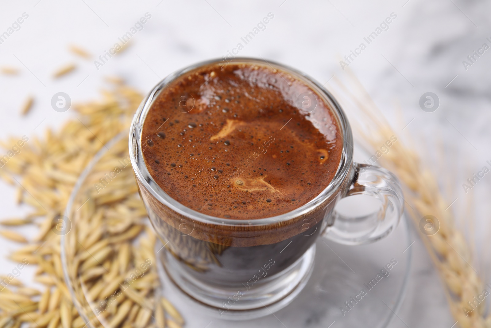 Photo of Cup of barley coffee, grains and spike on light table, closeup