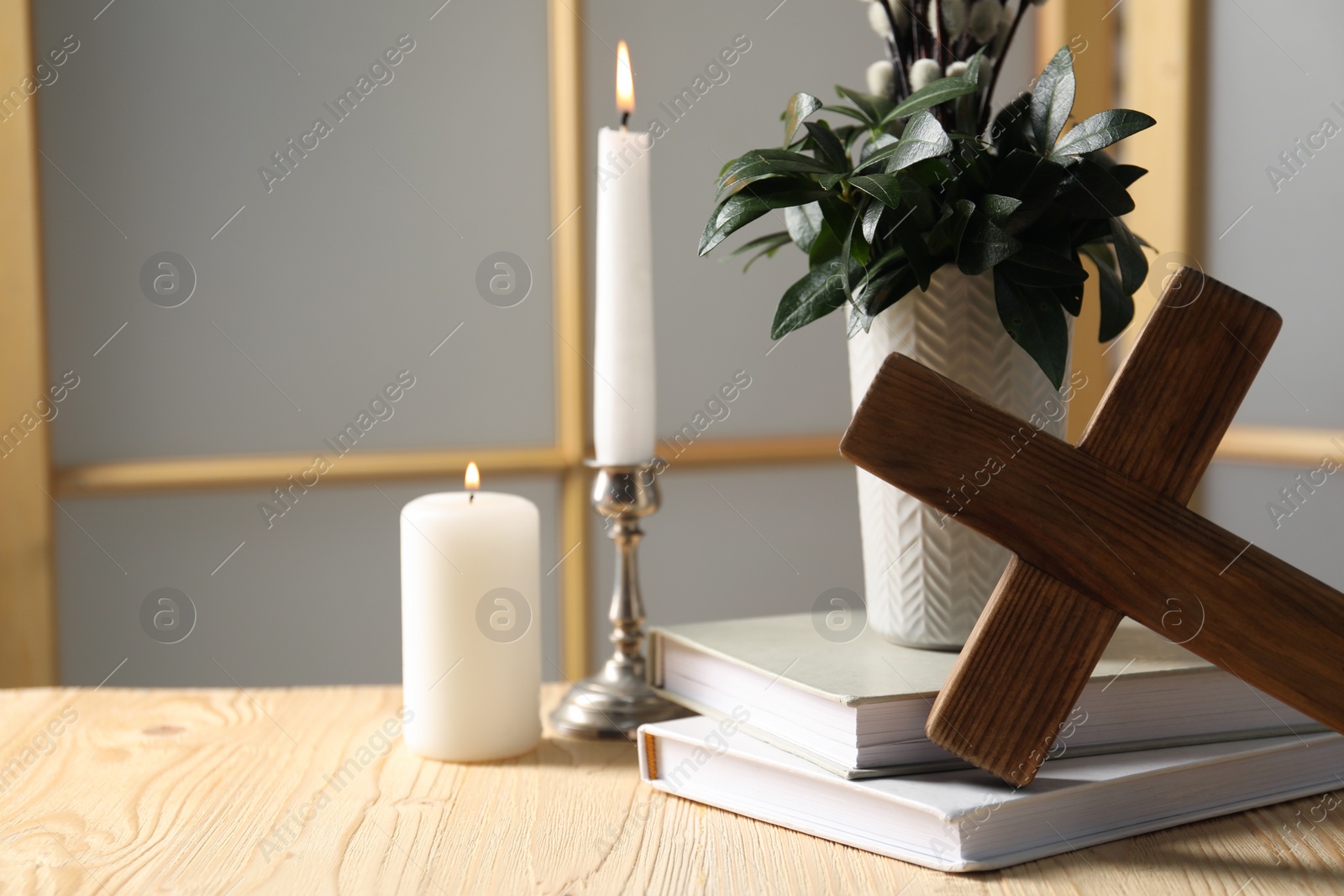 Photo of Cross, burning candles, books and bouquet with willow branches on wooden table