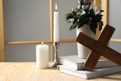 Photo of Cross, burning candles, books and bouquet with willow branches on wooden table