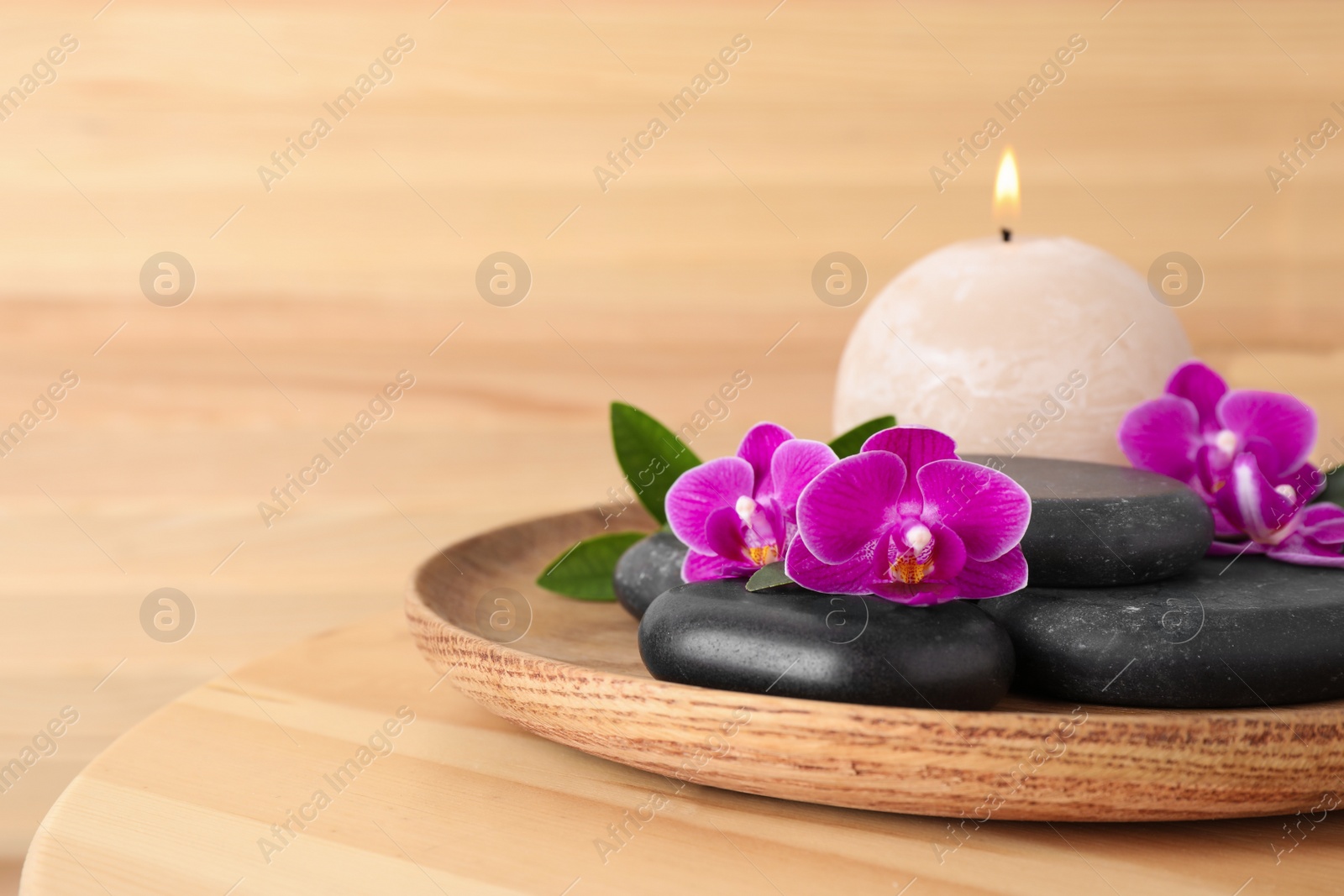 Photo of Tray with spa stones, orchid flowers and candle on wooden table. Space for text