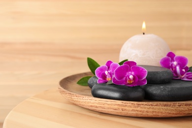 Photo of Tray with spa stones, orchid flowers and candle on wooden table. Space for text