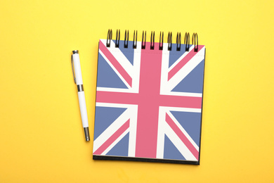 Image of Stylish notebook and pen on yellow background, top view. Learning English