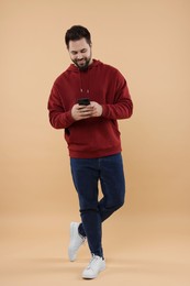 Happy young man using smartphone on beige background