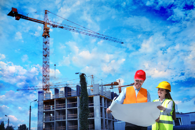 Professional engineers in safety equipment with drafting at construction site
