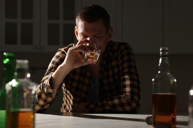 Addicted man drinking alcohol at table in kitchen