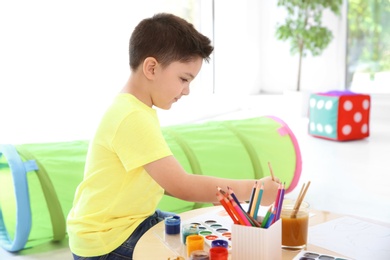 Photo of Cute little child painting at table in playing room