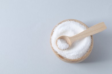 Photo of Organic white salt in bowl and spoon on light grey background, top view. Space for text