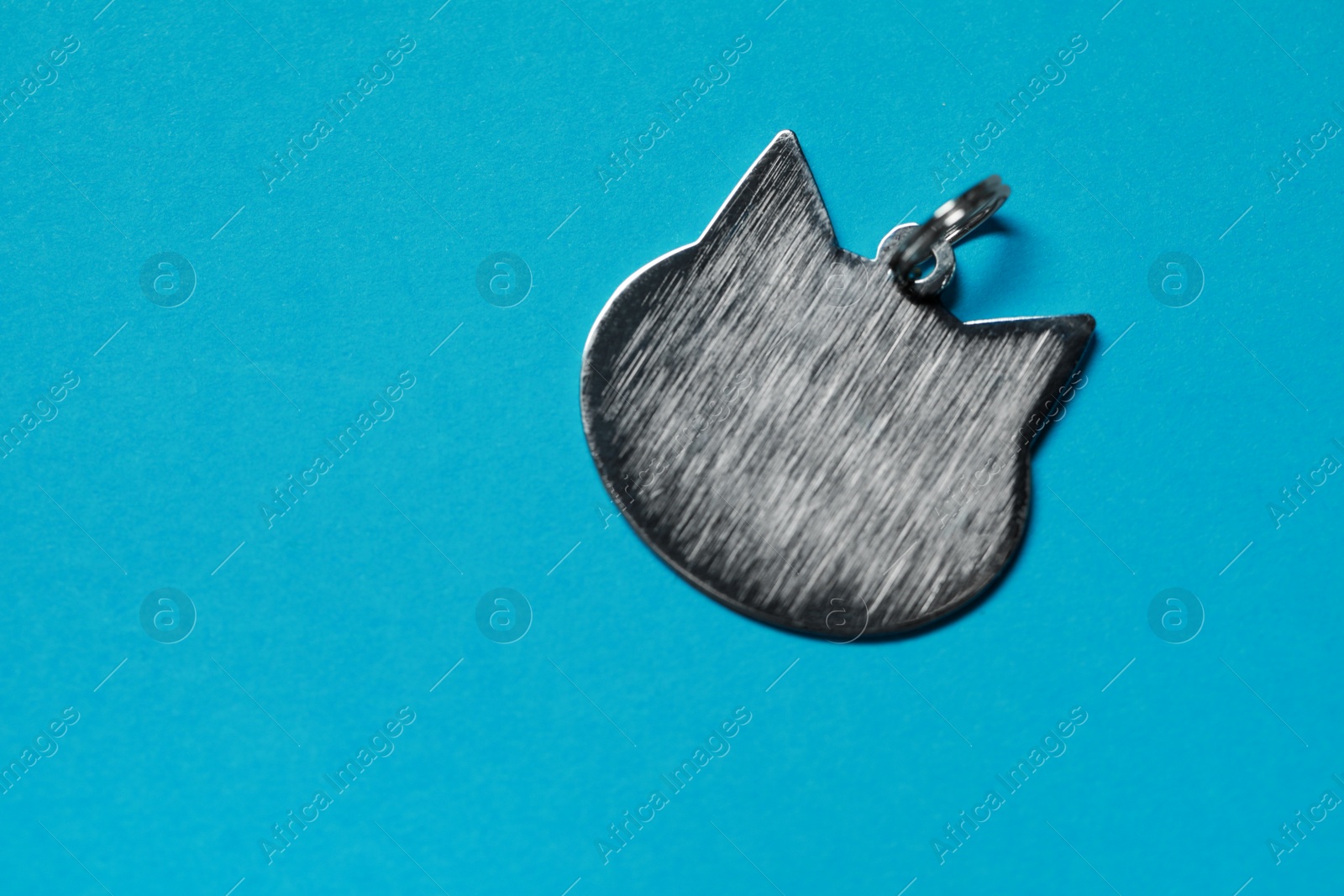 Photo of Silver pet tag in shape of cat with ring on light blue background, top view. Space for text